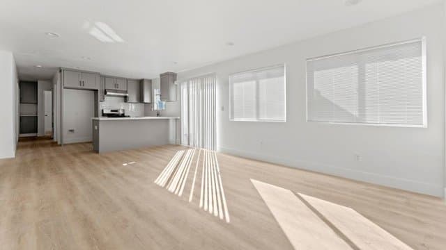 Empty open-concept living room and kitchen with light wood-look flooring and gray cabinets